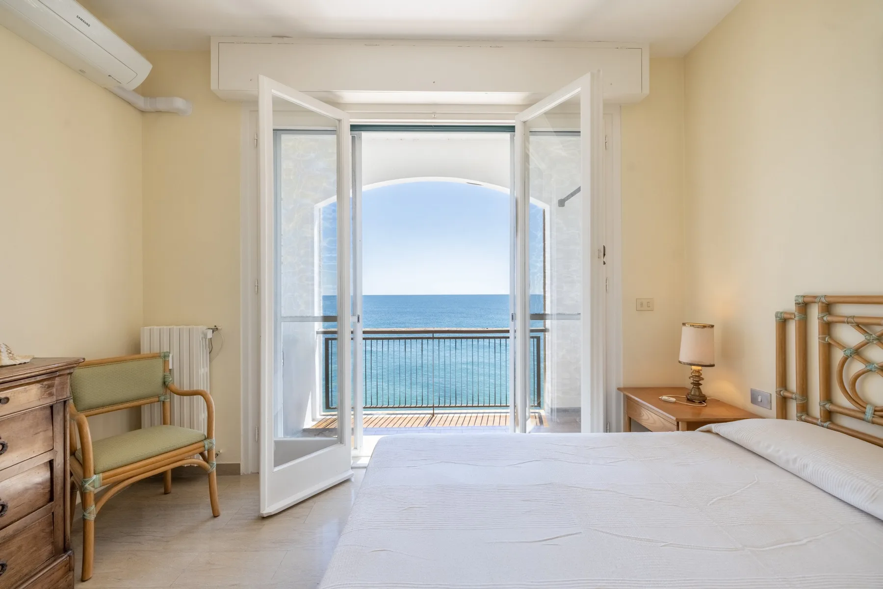 Un dormitorio con la puerta del balcón abierta y vista al mar.