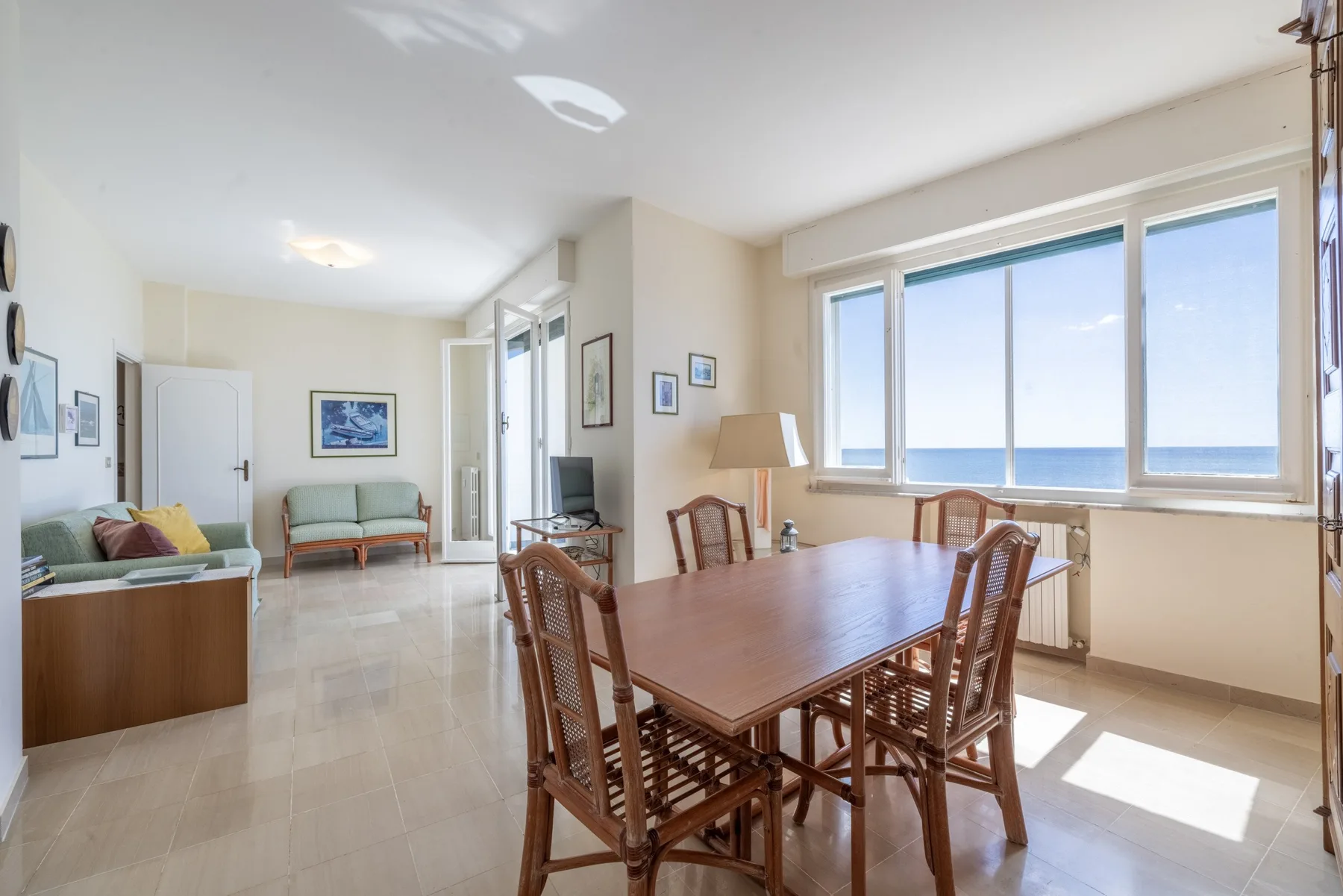 Un comedor luminoso con una mesa de madera junto a grandes ventanas con vistas al mar.