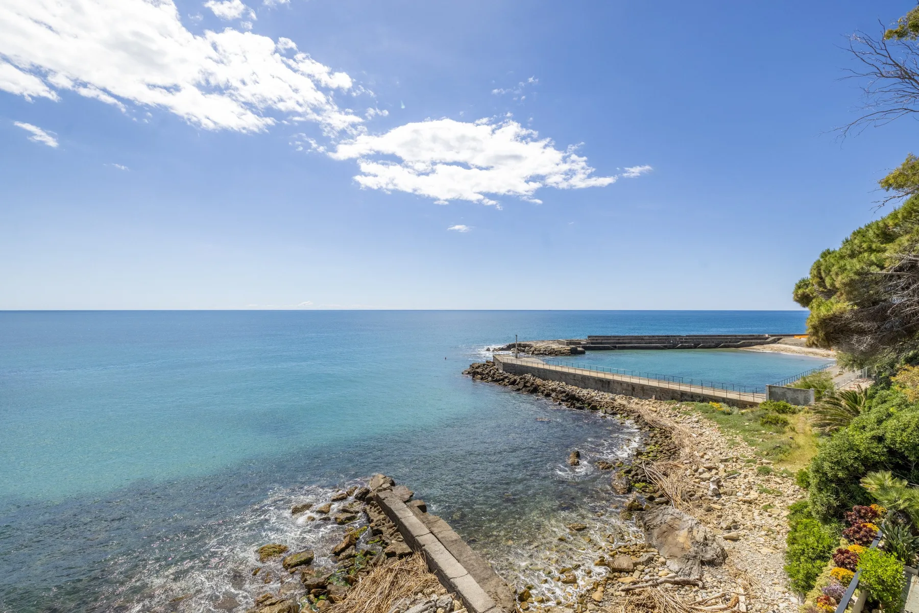 Una costa rocosa se encuentra con aguas azules tranquilas bajo un cielo parcialmente nublado.