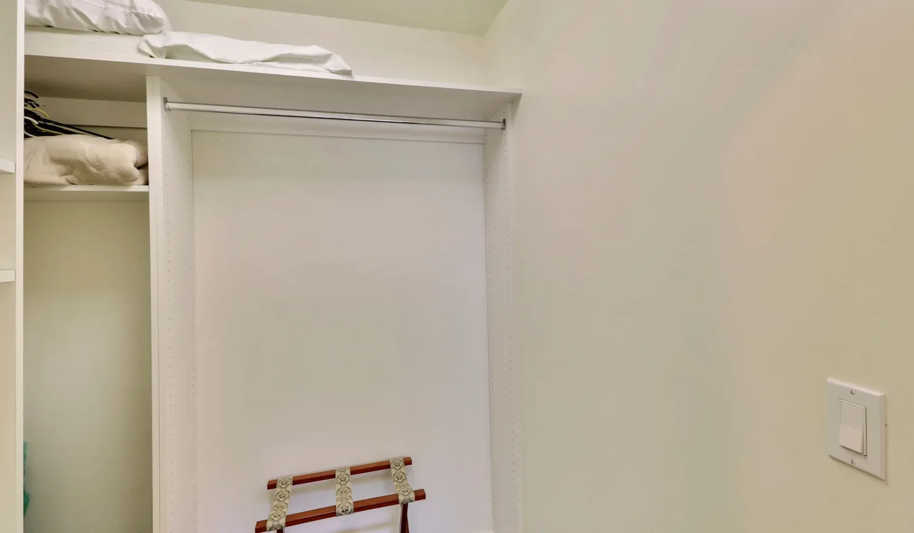 Un armario de dormitorio tiene estantes abiertos y una barra para colgar.