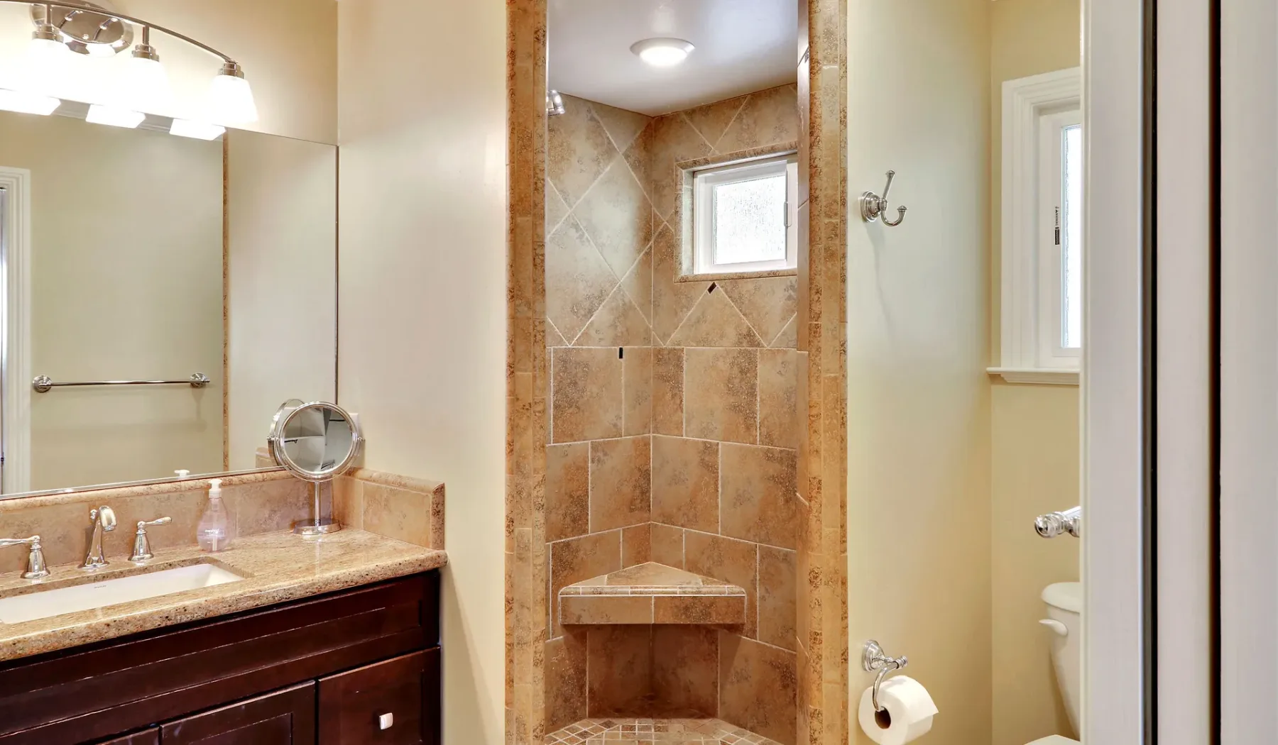 Un baño con ducha revestida de azulejos, lavabo con mueble y espejo grande.