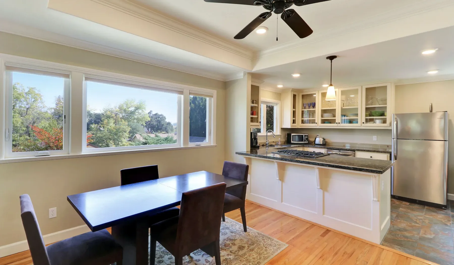Un comedor se abre a una cocina con una isla central y grandes ventanas.