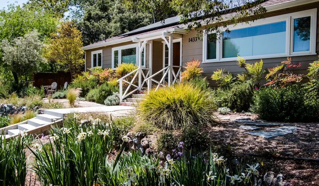 Una casa de una planta se encuentra entre jardines y árboles frondosos.