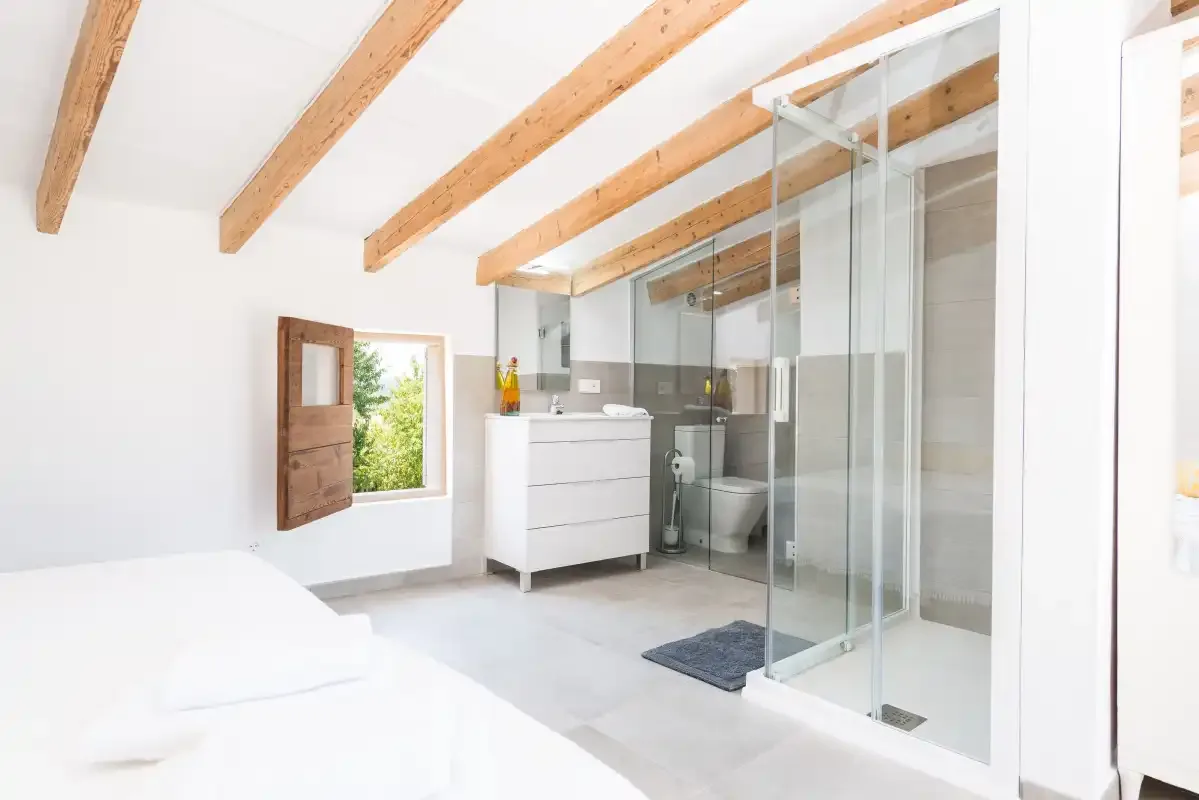 A bright bedroom with a bed beside a glass-enclosed shower.