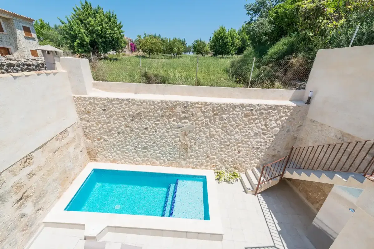 An outdoor swimming pool sits beside a stone wall and steps.