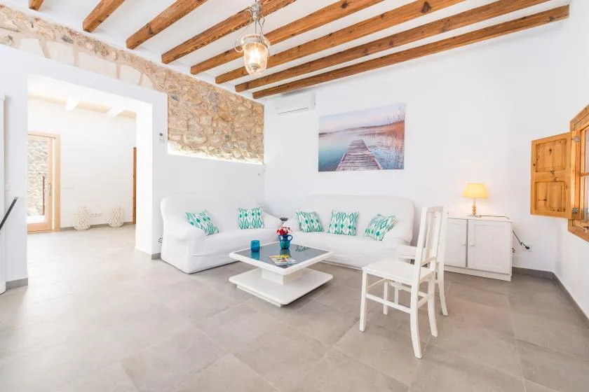 A bright living room with white seating, a coffee table, and exposed ceiling beams.