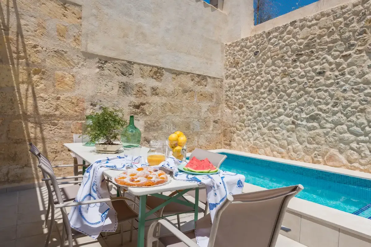A courtyard pool beside a dining table set with food and drinks.