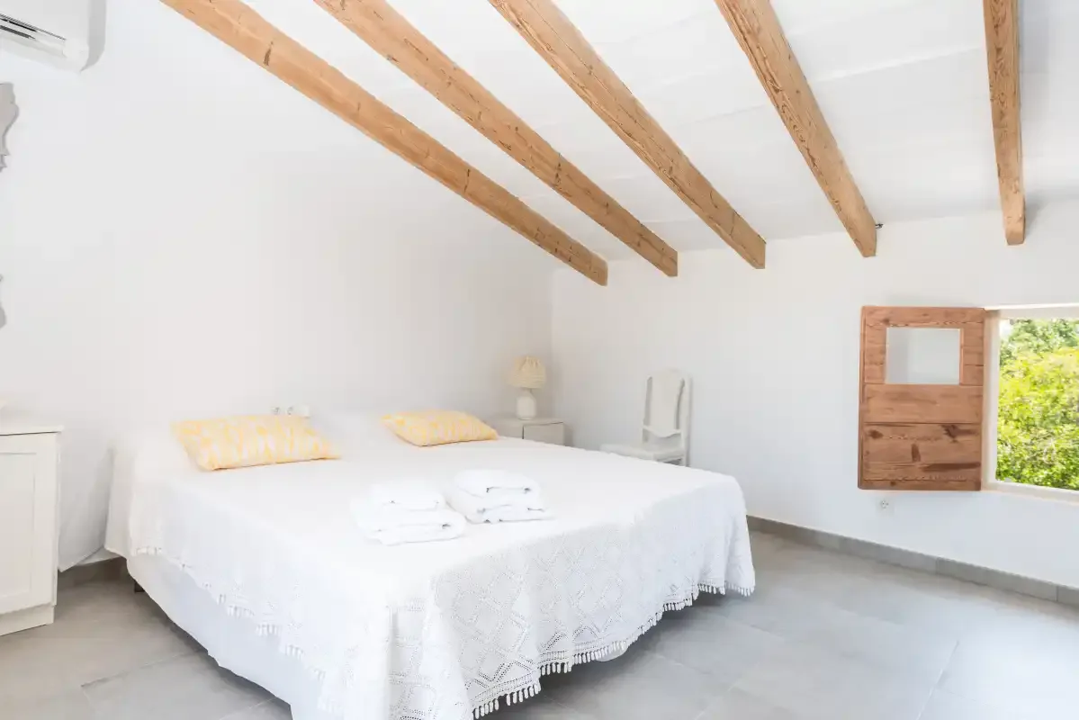A bright bedroom with a bed beneath exposed wooden ceiling beams.
