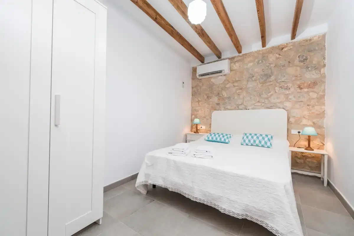 A bright bedroom with a neatly made bed beneath exposed ceiling beams.