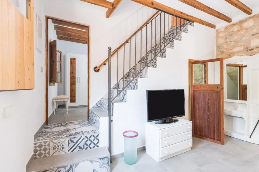 A bright interior with a tiled staircase, television, and wooden beams.