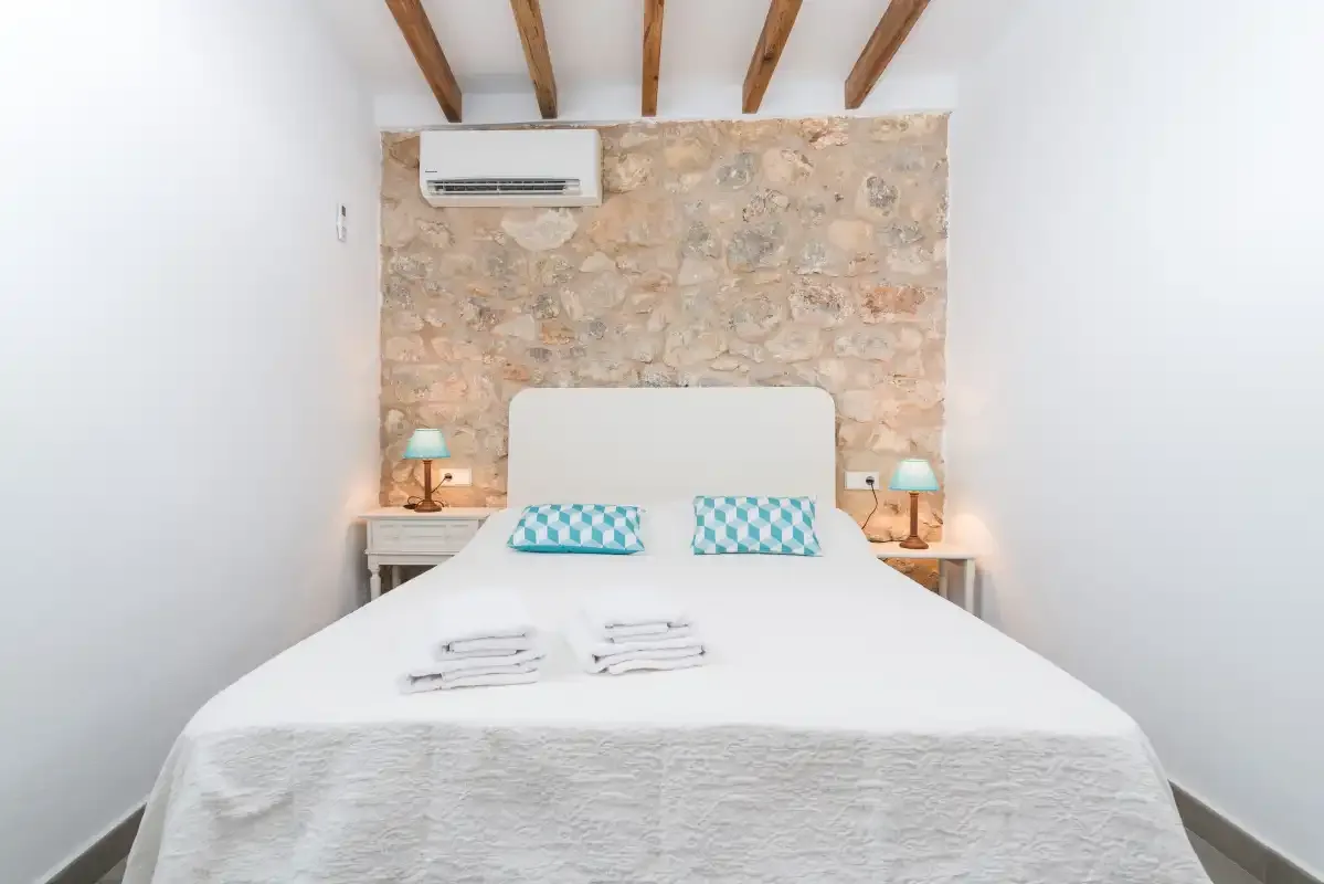 A bright bedroom features a white bed against a stone accent wall.
