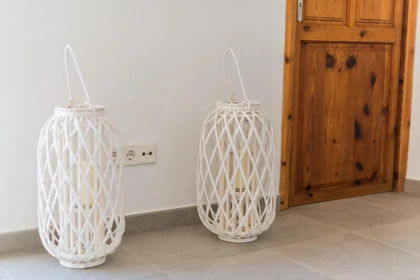 Two white woven decorative lanterns stand beside a wooden cabinet in a tiled room.