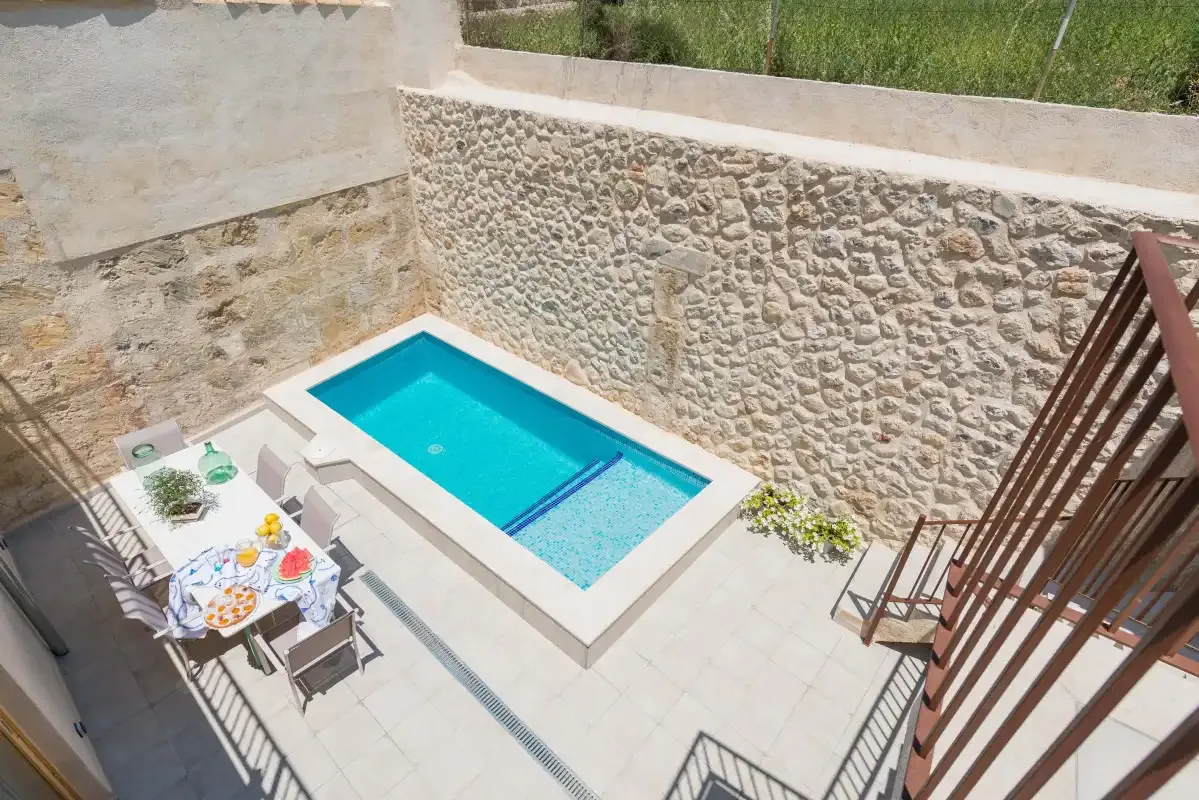 A small outdoor pool sits beside a paved patio and stone wall.