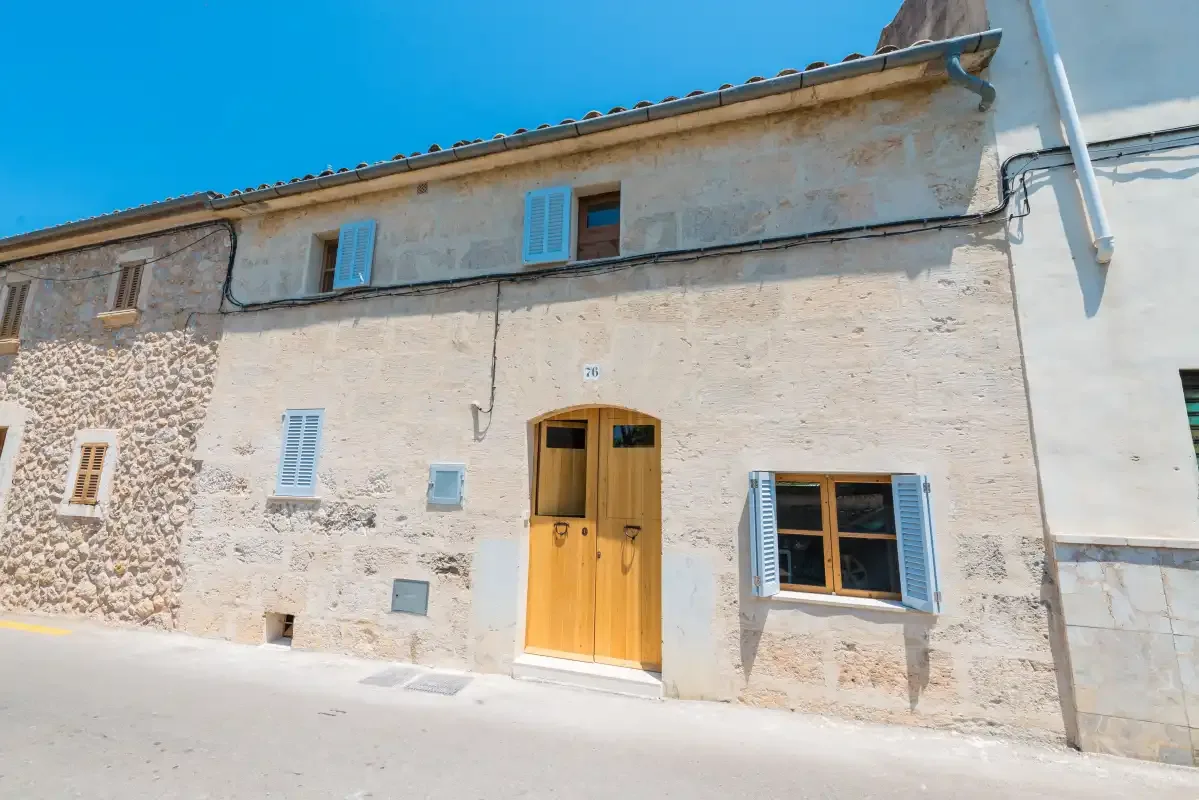 A stone-fronted building with a wooden entrance door and blue shutters.