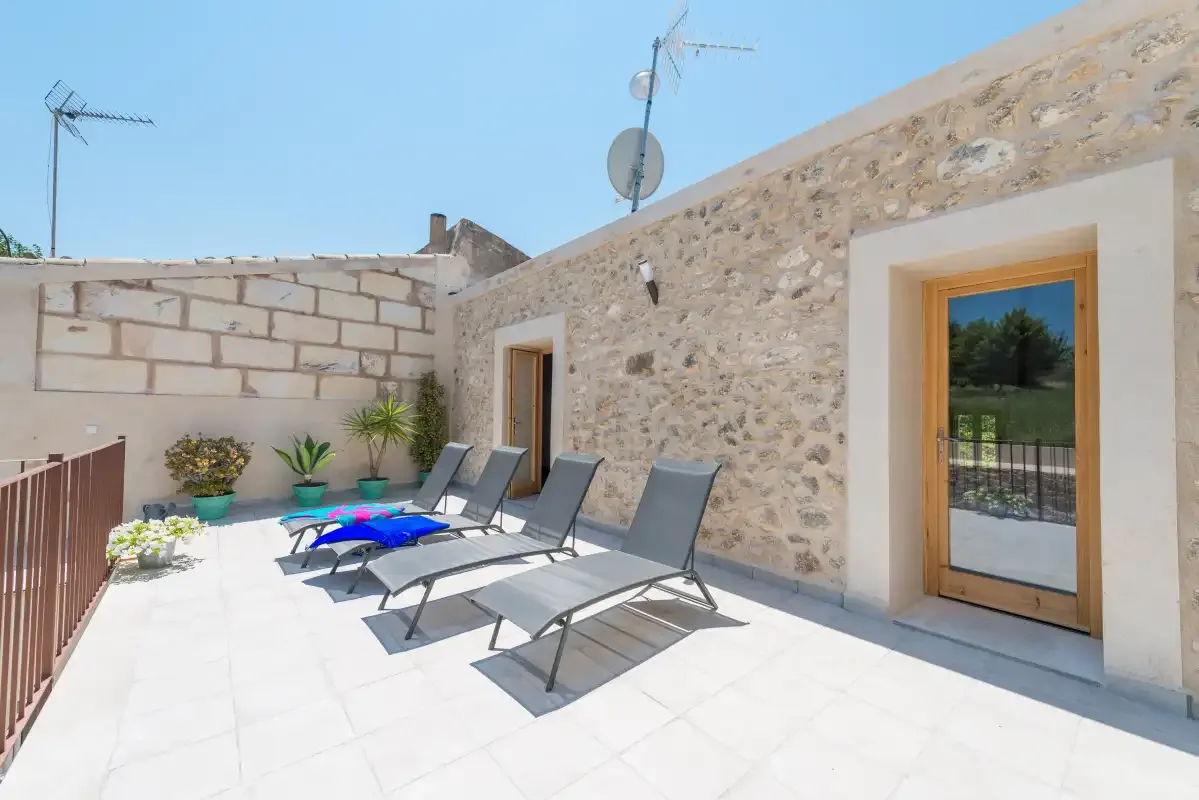 A sunlit stone terrace has several lounge chairs and potted plants.