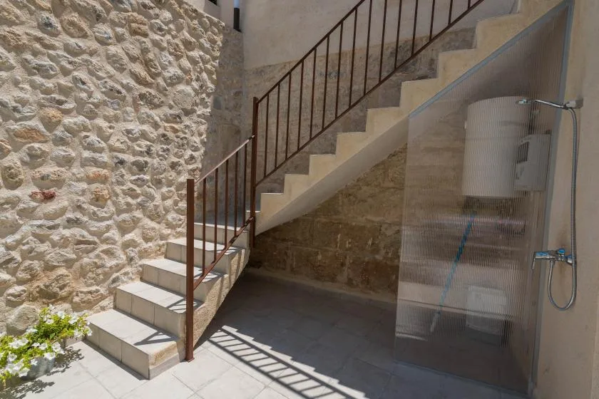 An outdoor stairway runs beside a stone wall, with a shower area underneath.