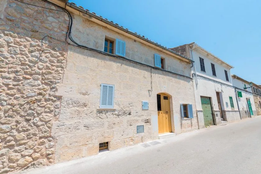 A sunlit stone building facade lines a quiet street under a clear blue sky.