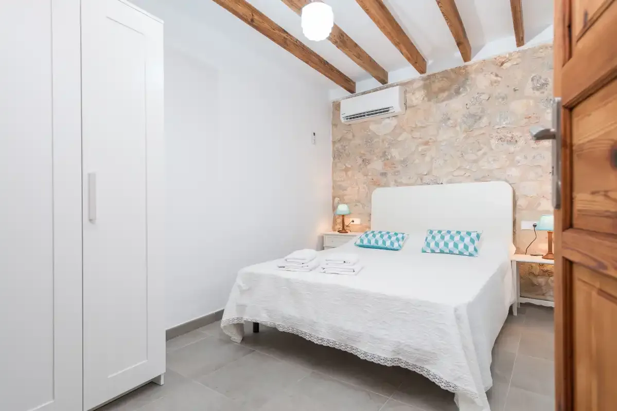 A bedroom with a neatly made bed and exposed wooden ceiling beams.