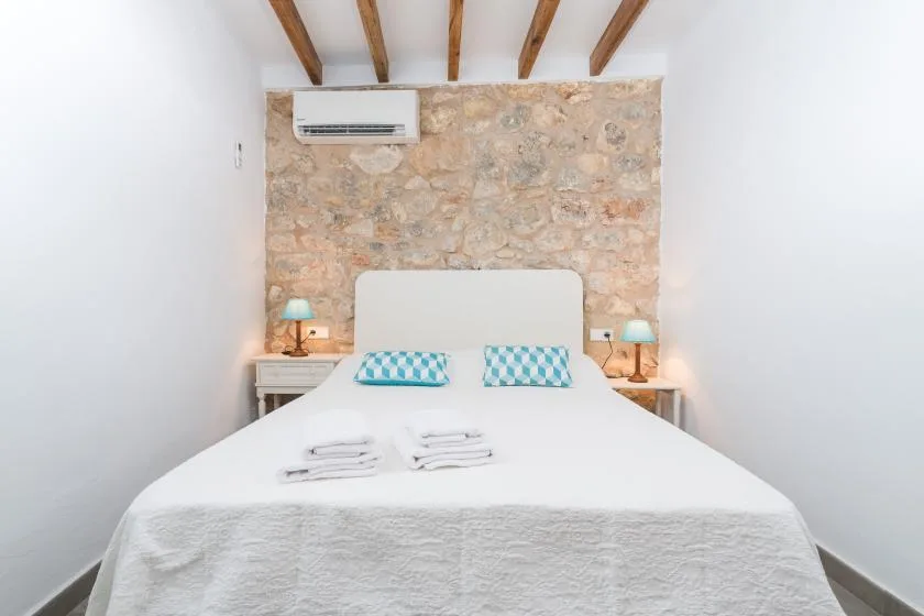 A bedroom with a white bed, turquoise pillows, and an exposed stone wall.