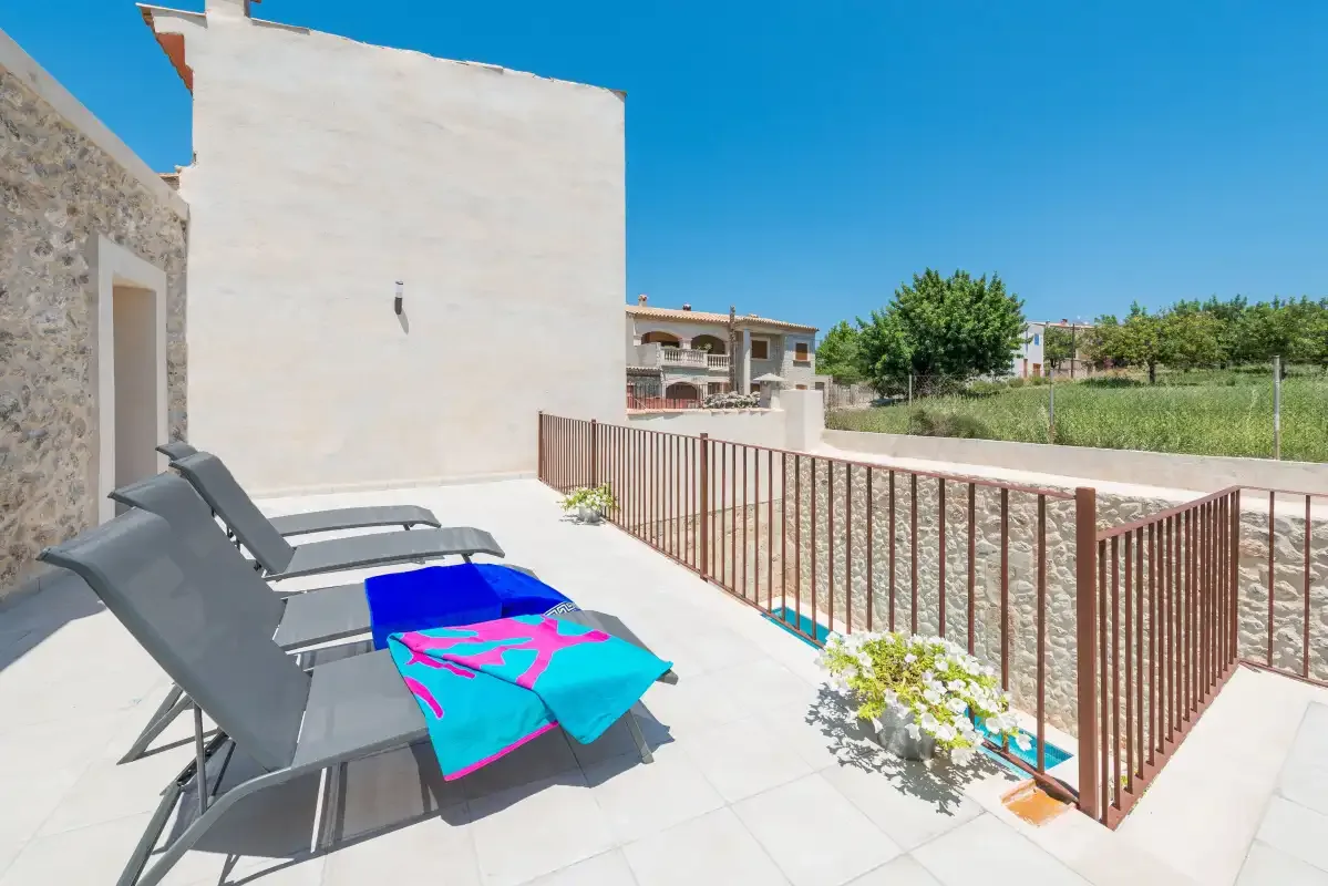 A sunny outdoor terrace has reclining seating beside a metal railing.