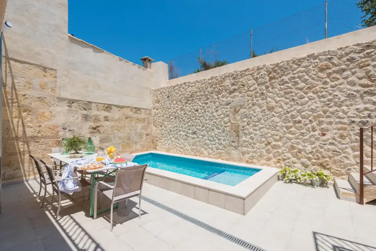 A small outdoor pool sits beside a dining table in a stone-walled courtyard.
