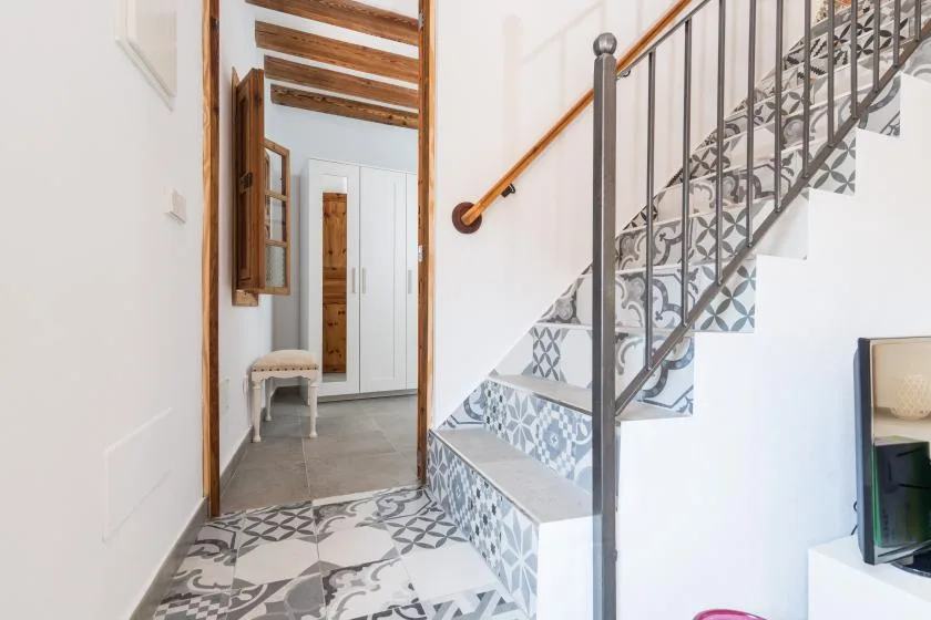 A patterned tiled staircase rises beside a bright hallway.