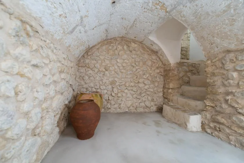 A stone room with a rounded ceiling, an earthenware jar, and steps.