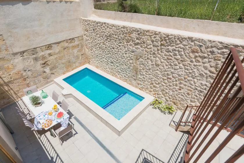 A small outdoor pool sits beside a stone wall and a paved patio.
