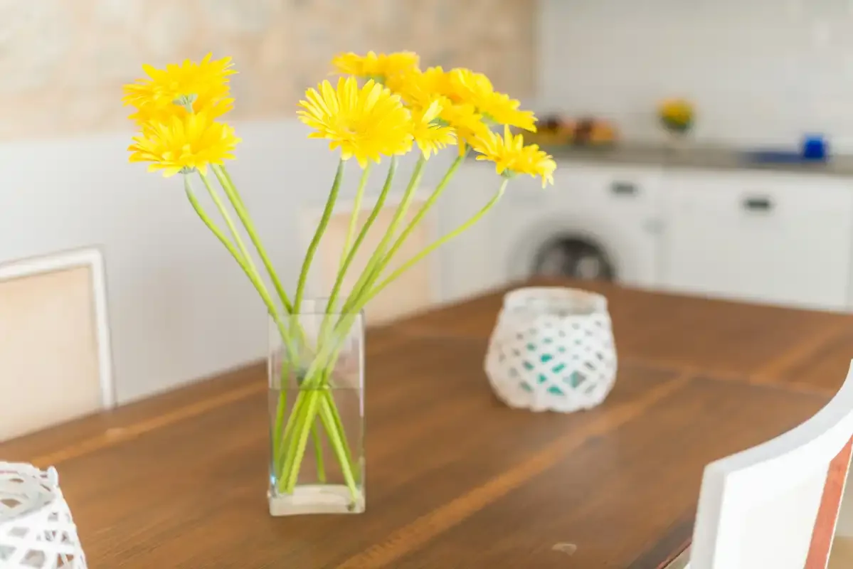 A dining table with yellow flowers in a vase and white seating.