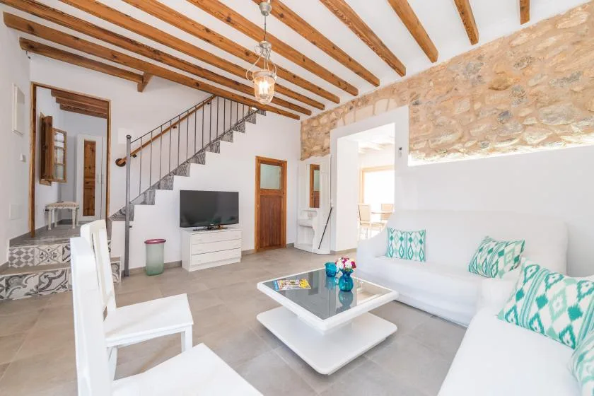 A bright living room with white seating, a low table, and exposed ceiling beams.