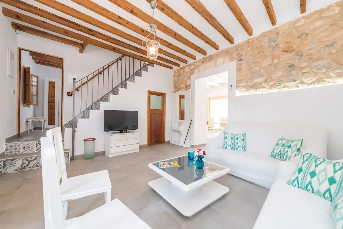 A bright living room has white seating, a coffee table, and exposed wooden ceiling beams.