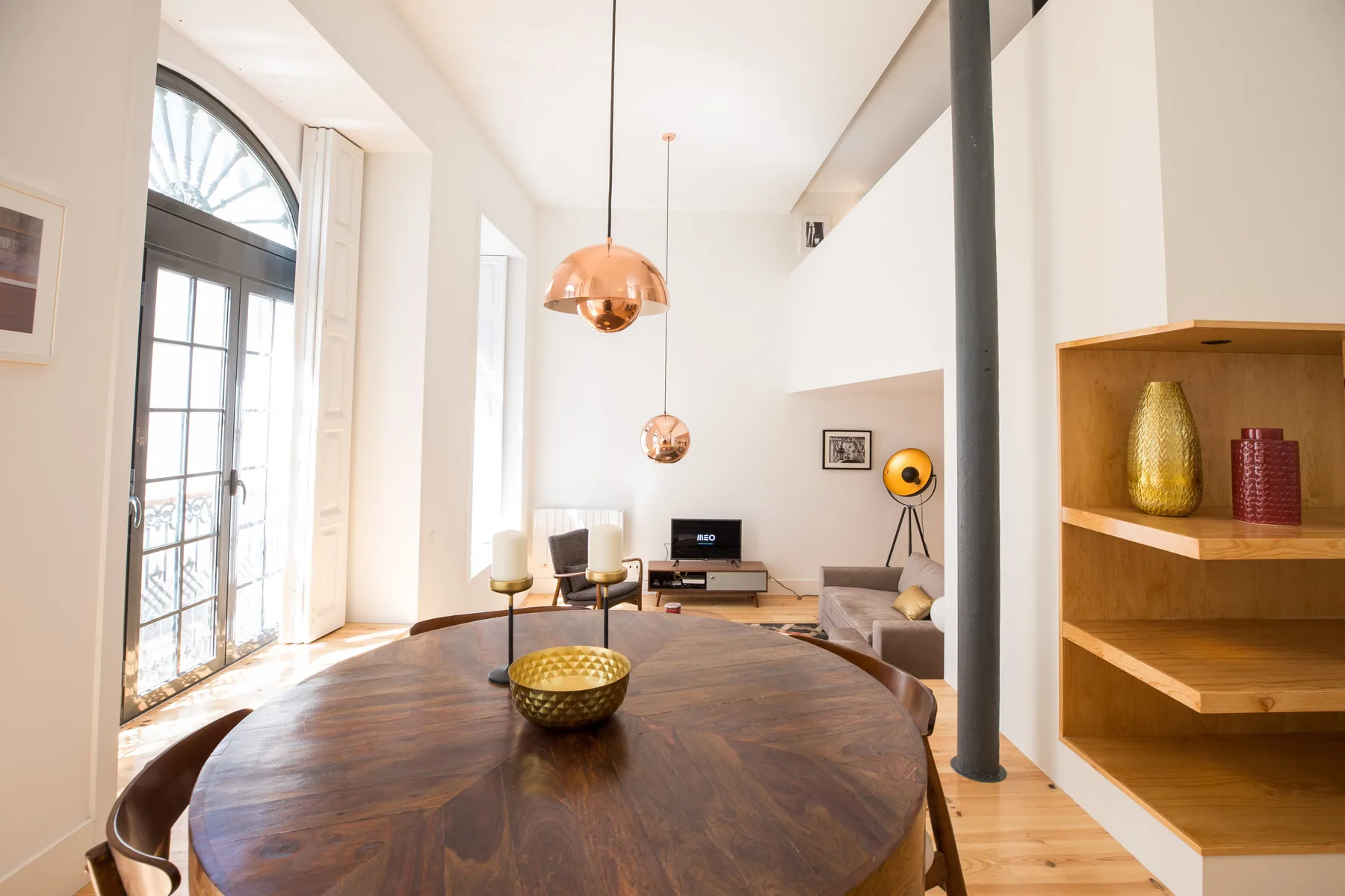 Sala de estar con mesa de comedor de madera, zona de asientos y ventanas altas.
