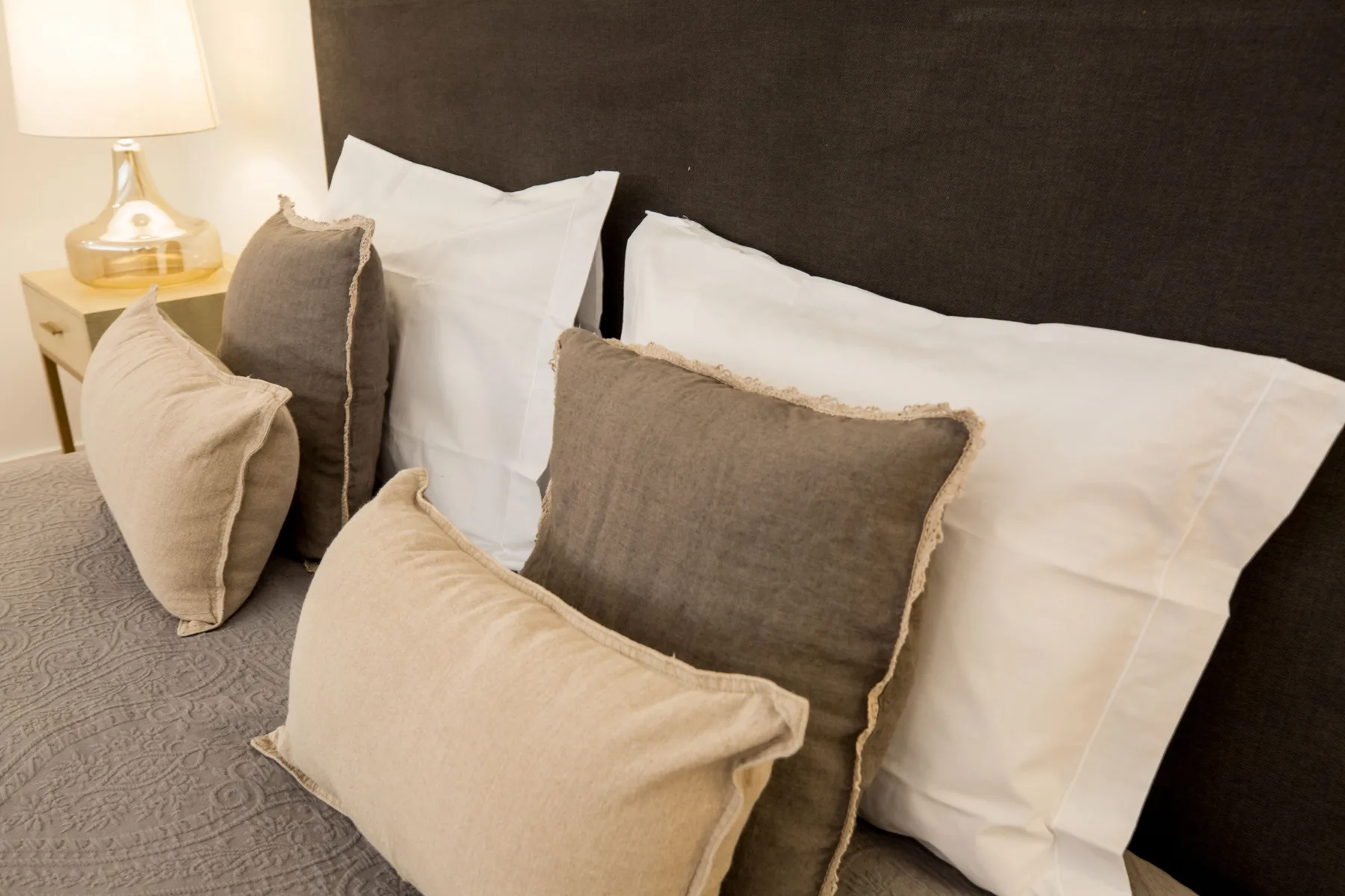 Dormitorio con almohadas de distintos tonos dispuestas sobre la cama.