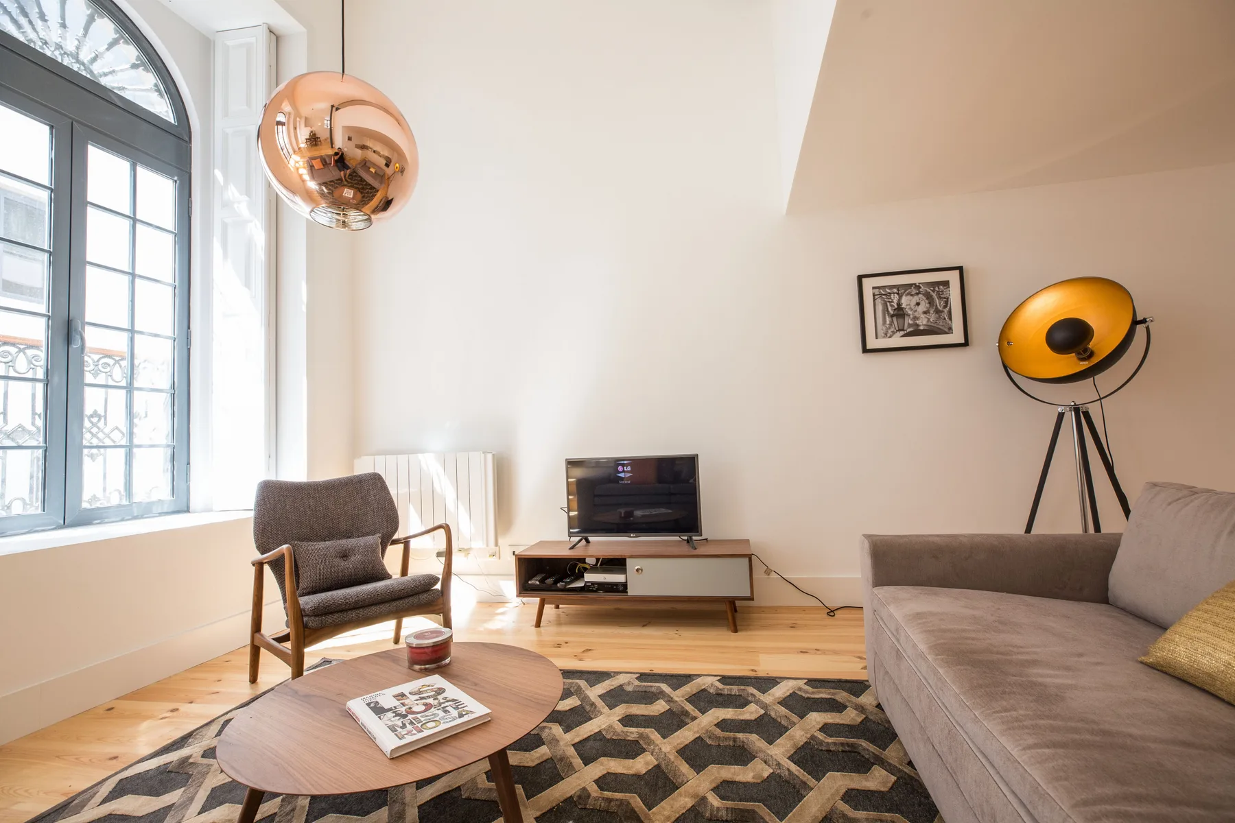 Sala de estar con asientos, un televisor y una gran ventana arqueada.