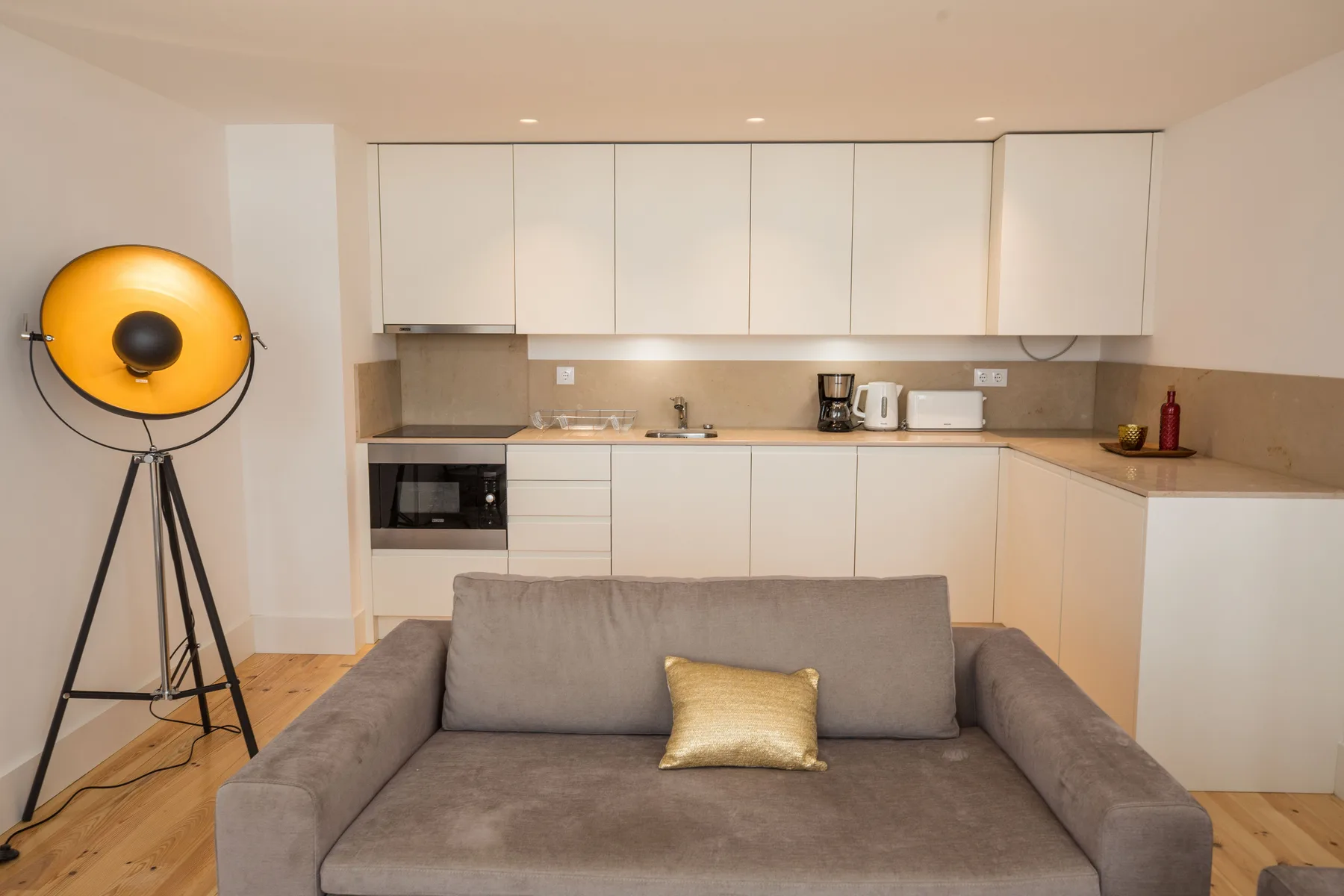 Sala de estar con asientos grises y una cocina al fondo.