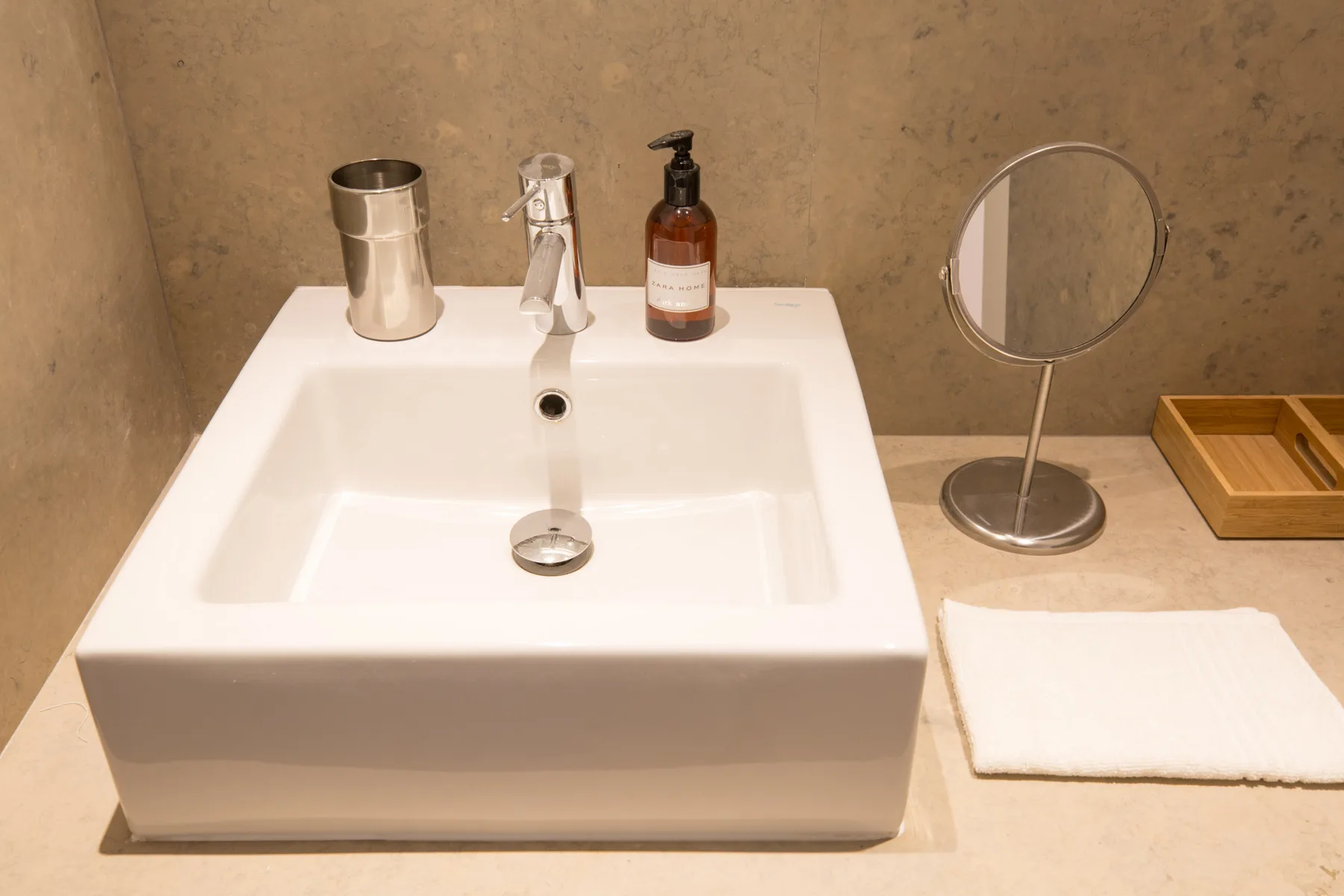 Un lavabo de baño está junto a un espejo de mesa pequeño y una toalla doblada.
