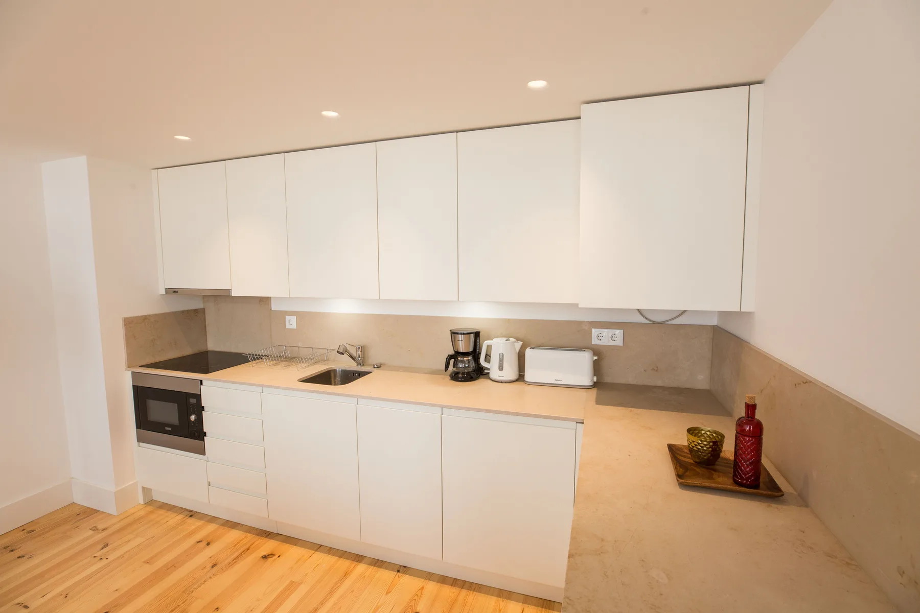 Una cocina moderna y luminosa con armarios blancos y pequeños electrodomésticos.