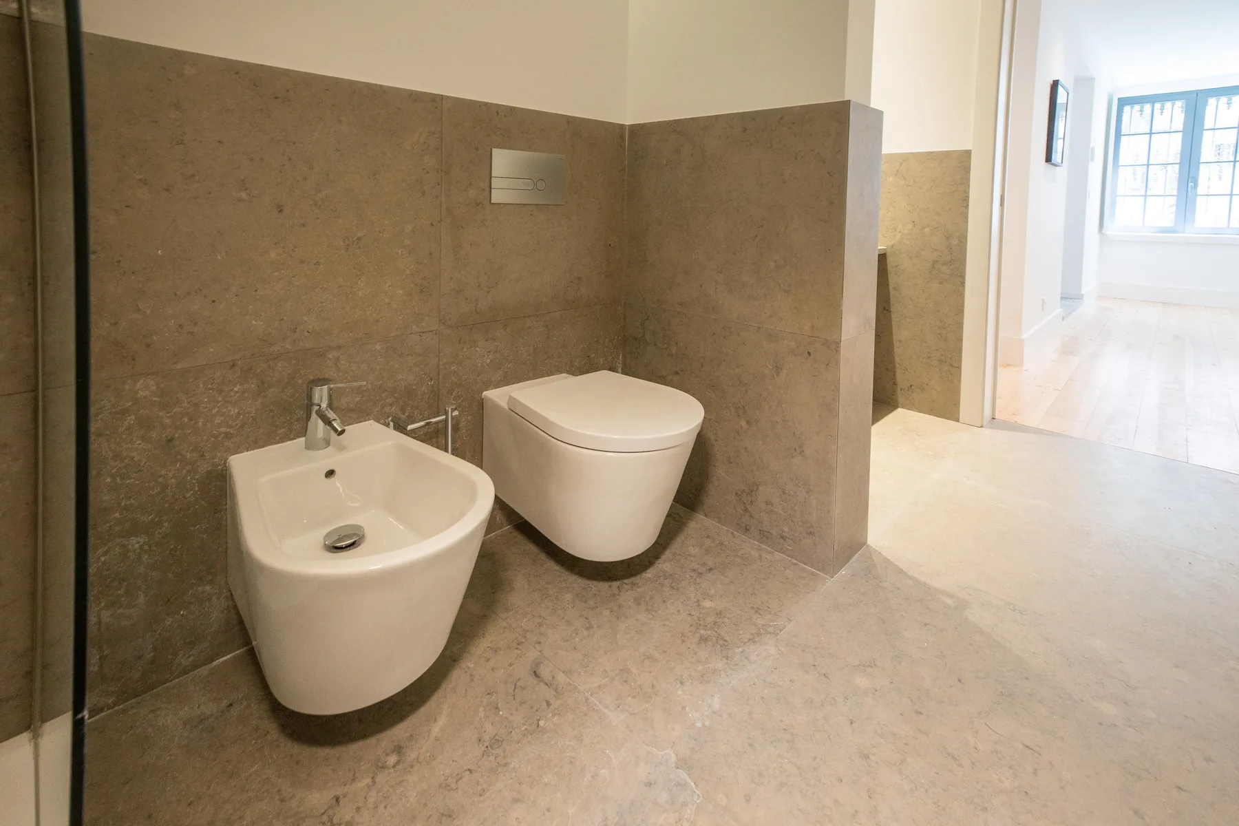 Un baño con inodoro y bidé junto a un pasillo luminoso.