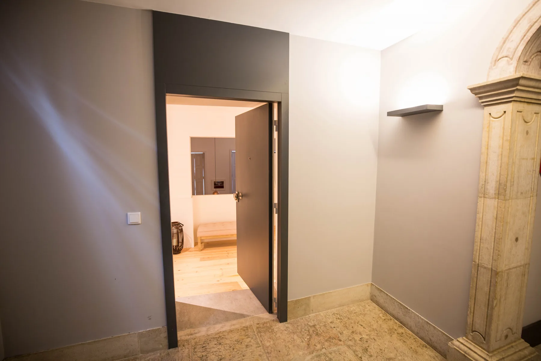 Un pasillo interior con una puerta abierta y suelo de piedra.