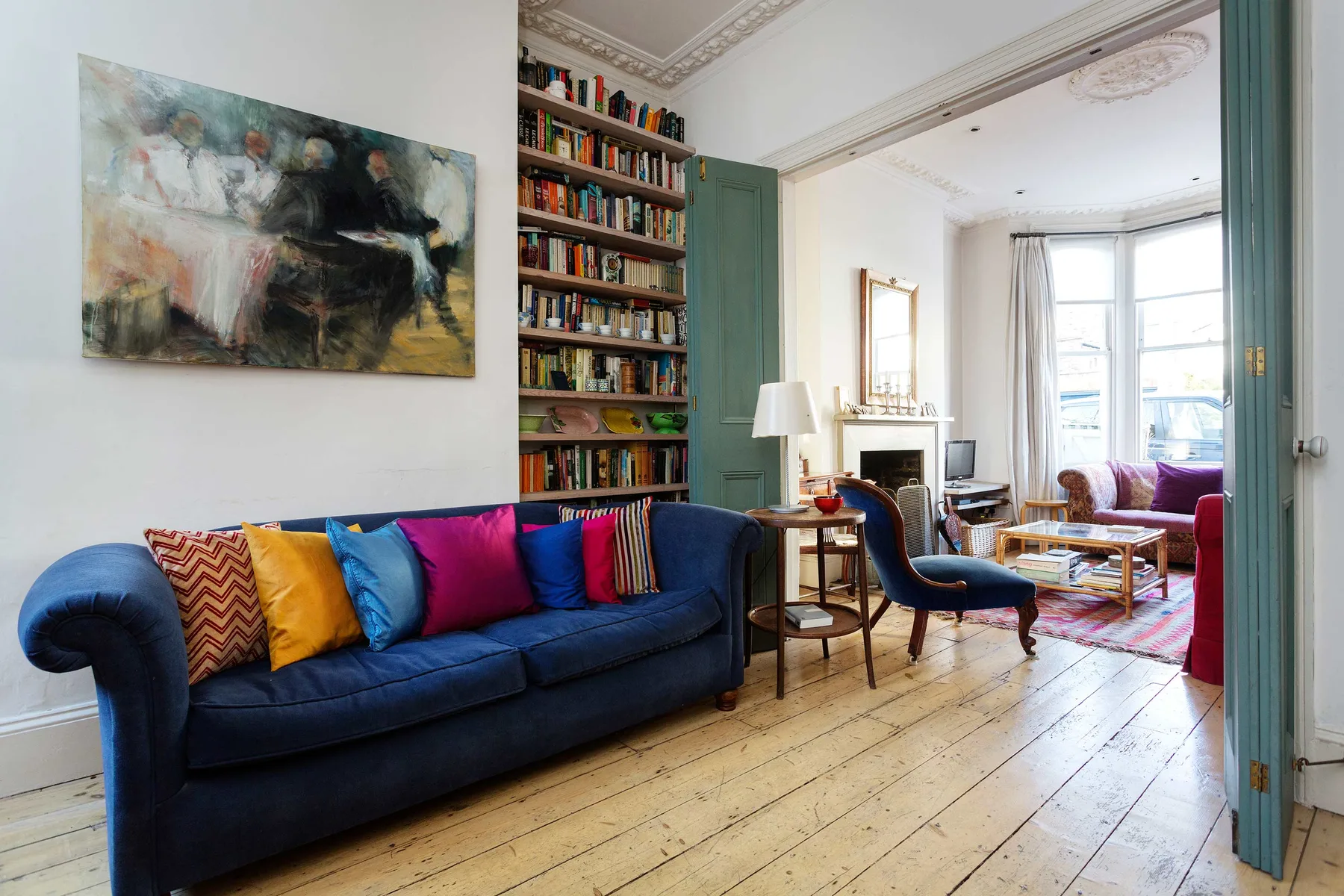 A bright living room with a blue sofa and a tall bookcase.