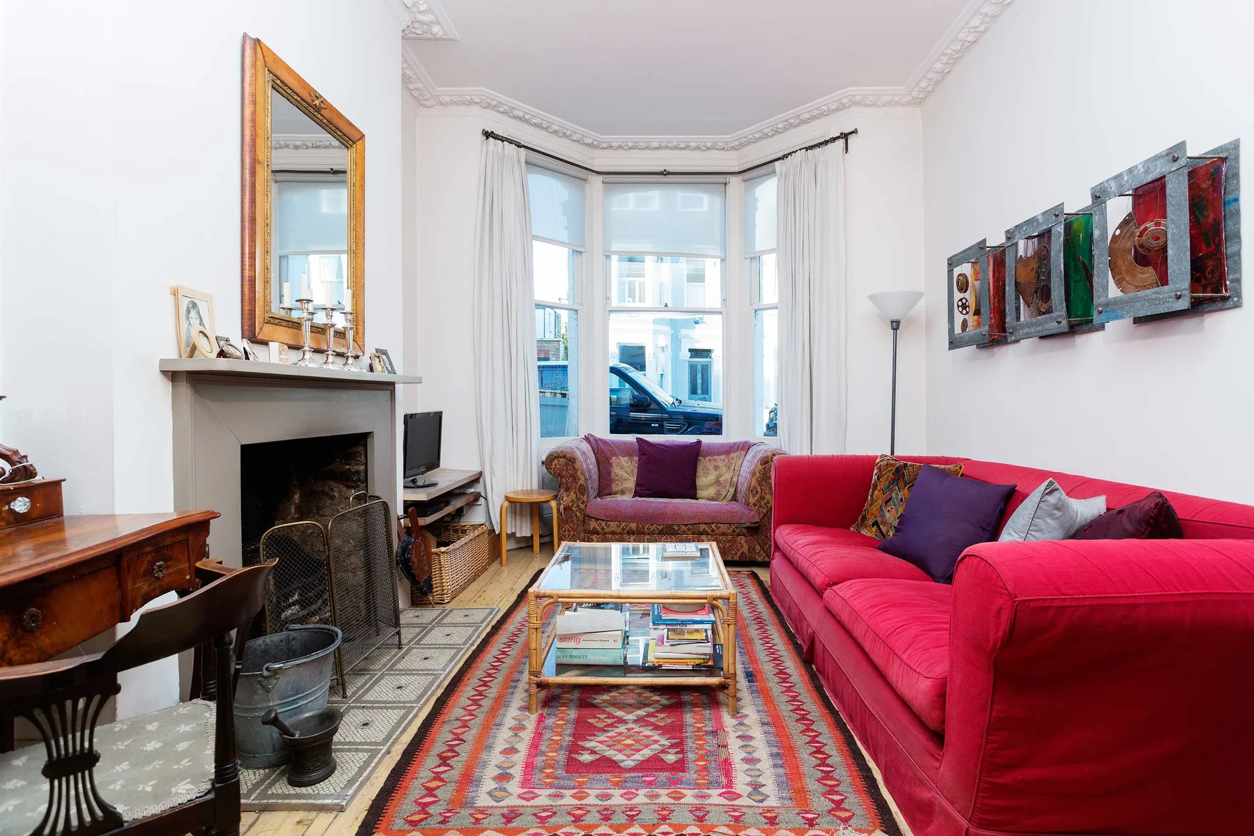 A bright living room with red seating, a fireplace, and a large bay window.