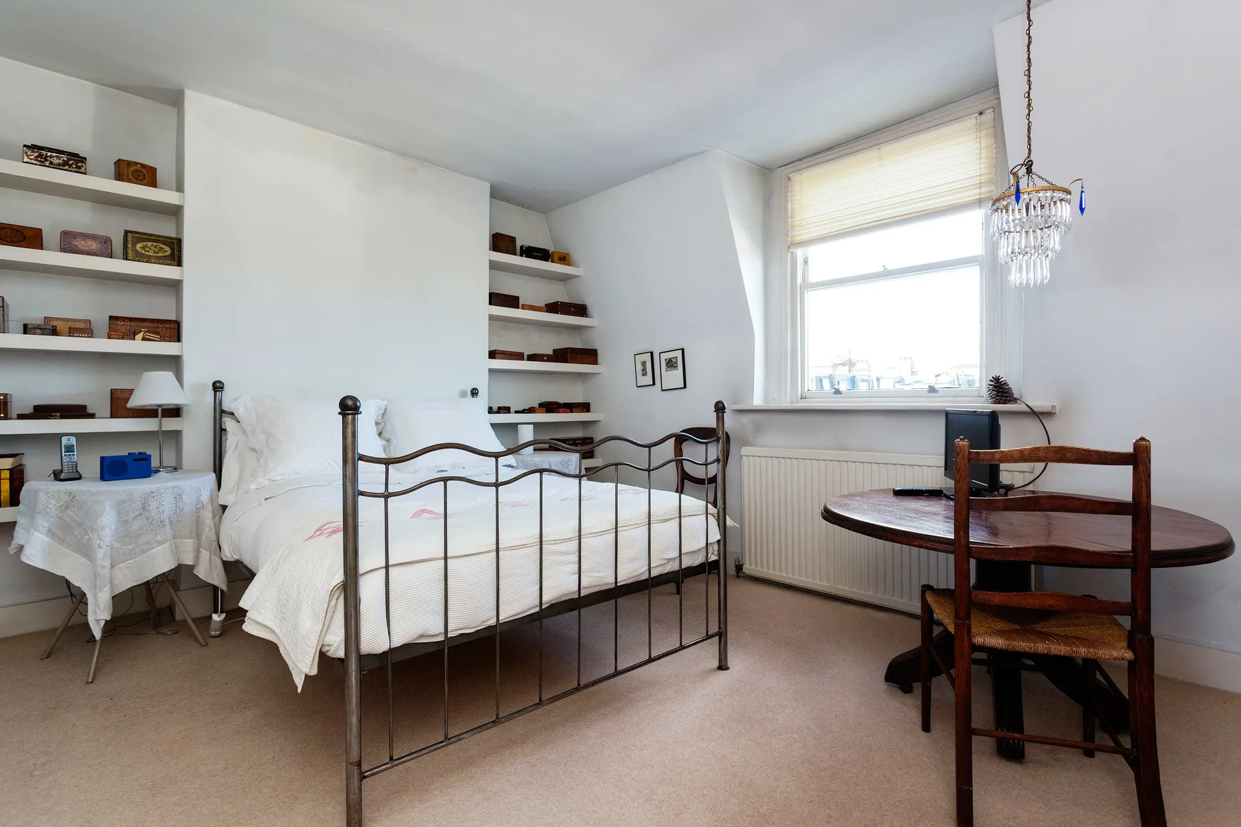 Un dormitorio con una cama, estantes empotrados y una mesa pequeña junto a la ventana.