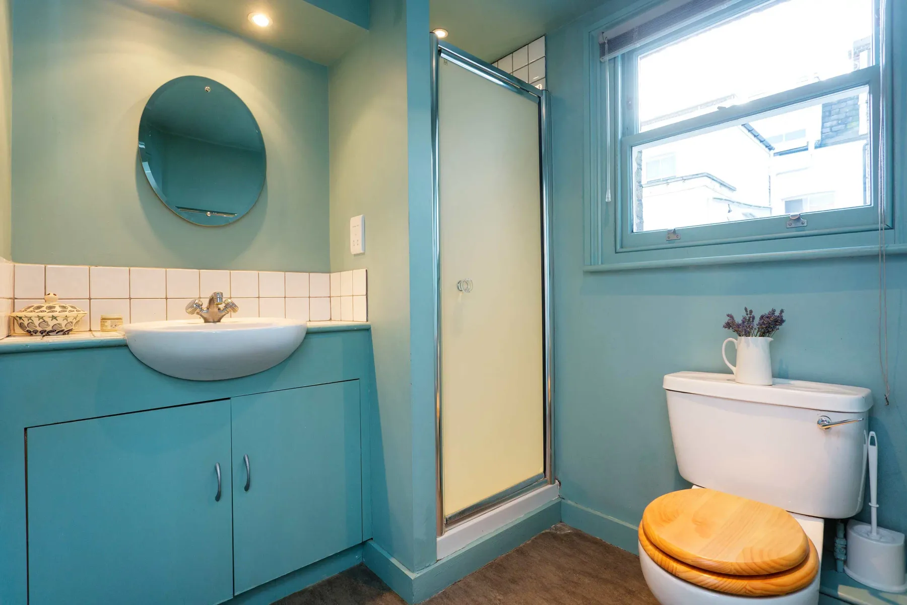 Un baño azul con lavabo, espejo redondo, ducha e inodoro.