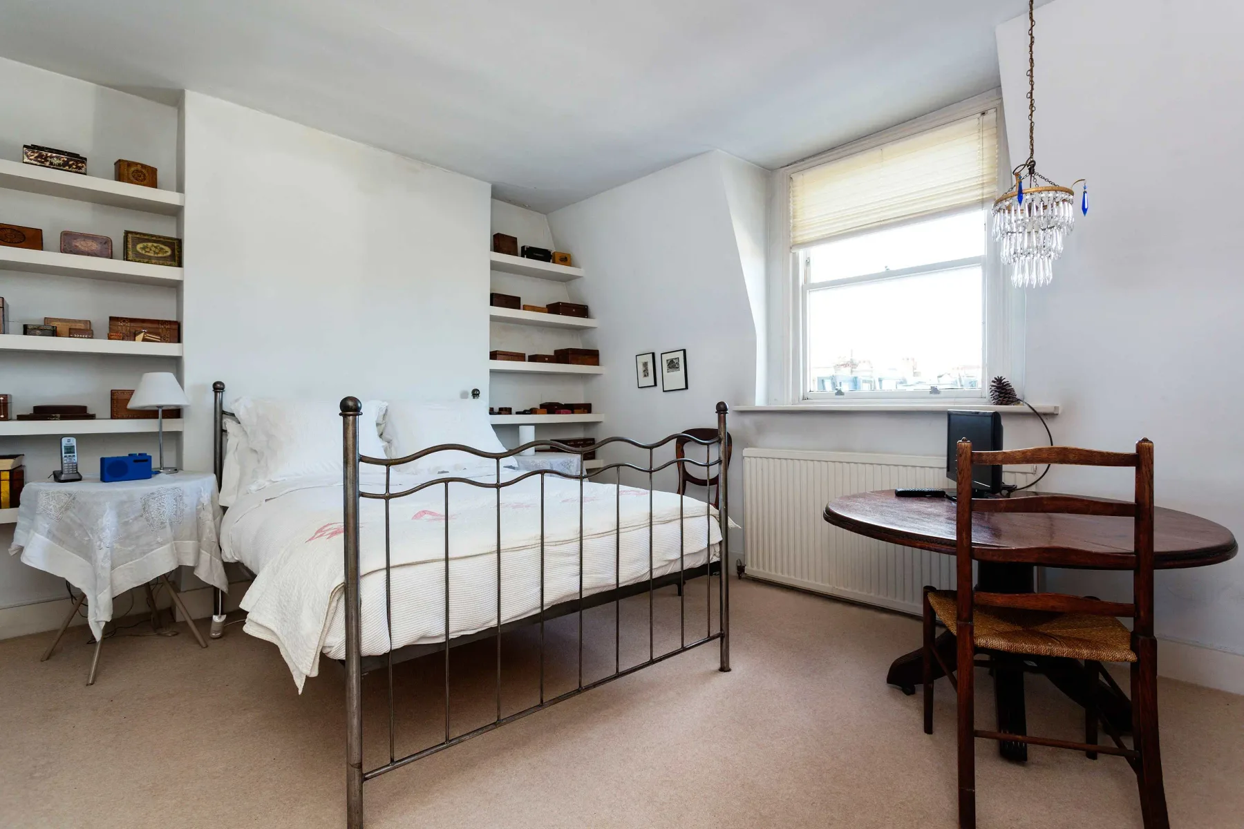 Un dormitorio luminoso con una cama, estantes empotrados y una mesa junto a la ventana.