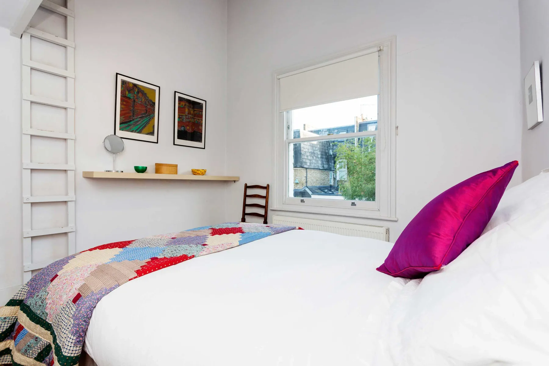 Un dormitorio luminoso con una cama, una colcha colorida y una ventana.