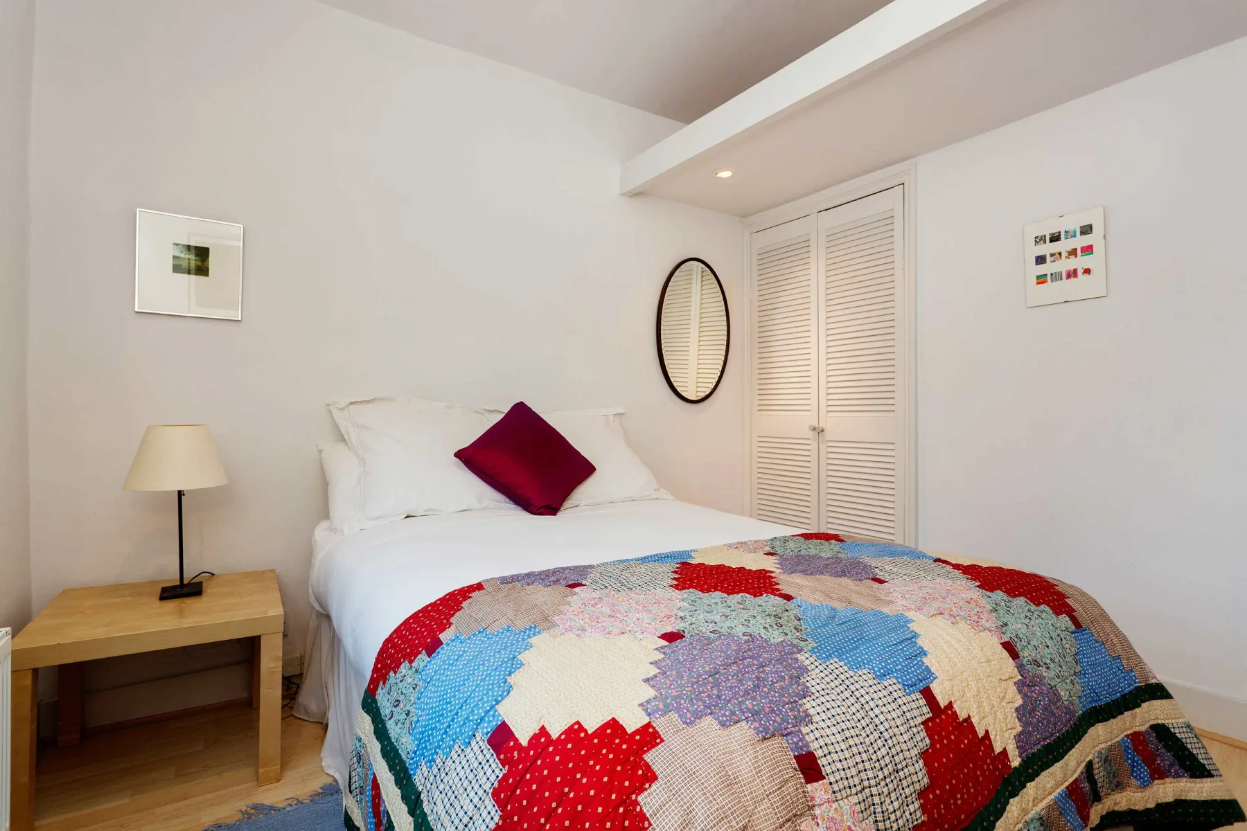 Un dormitorio con ropa de cama blanca y una colcha colorida de retazos.