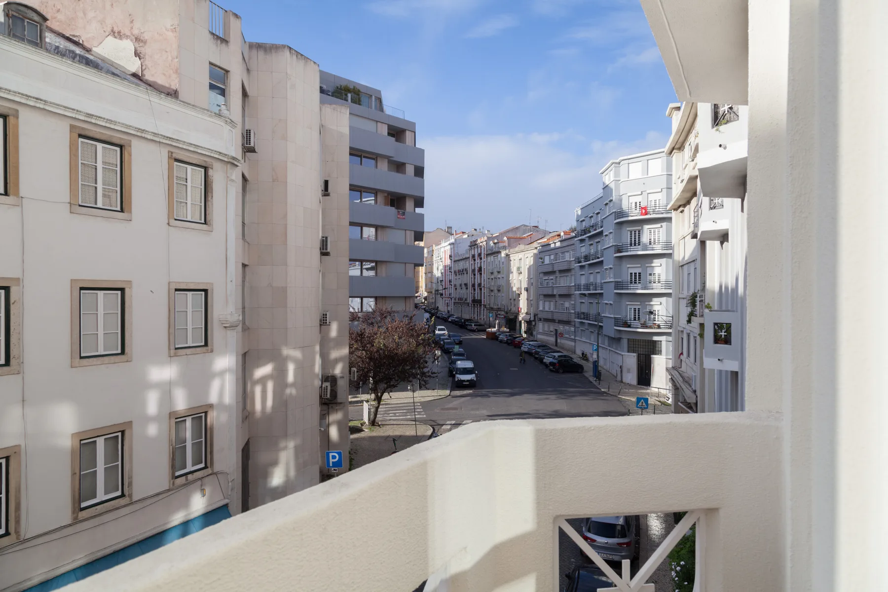 Una calle de la ciudad se ve desde un balcón, con edificios de apartamentos y coches aparcados.
