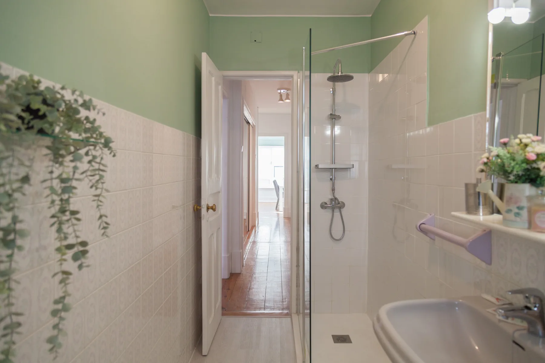 Un baño con ducha de vidrio, lavabo y una puerta abierta a un pasillo.
