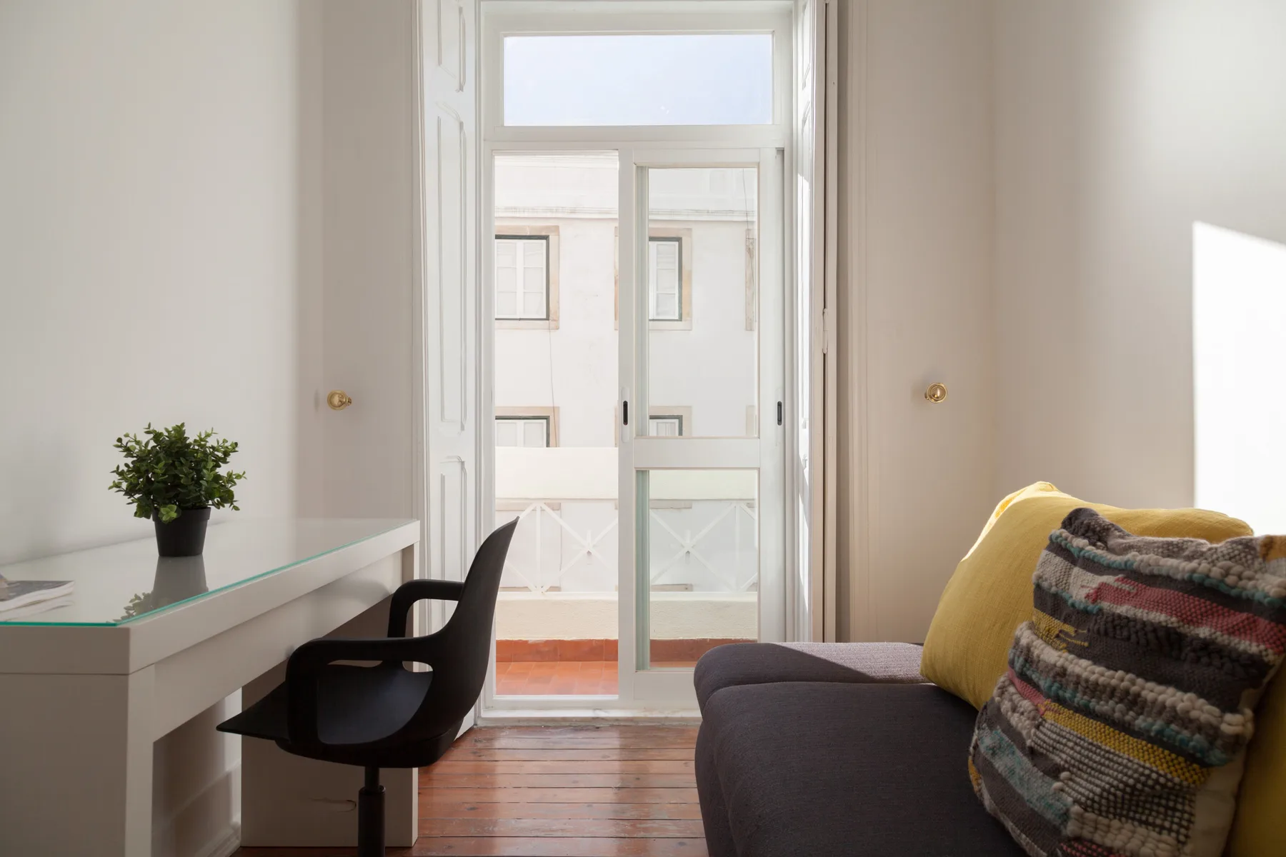 Sala de estar luminosa con un escritorio junto a puertas de vidrio altas y asientos.