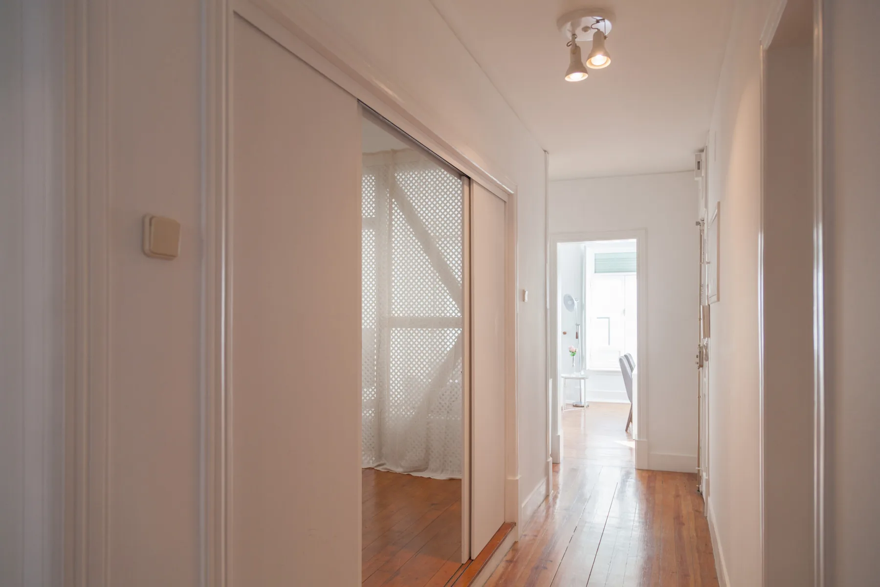 Un pasillo luminoso con suelo de madera y una puerta abierta al fondo.